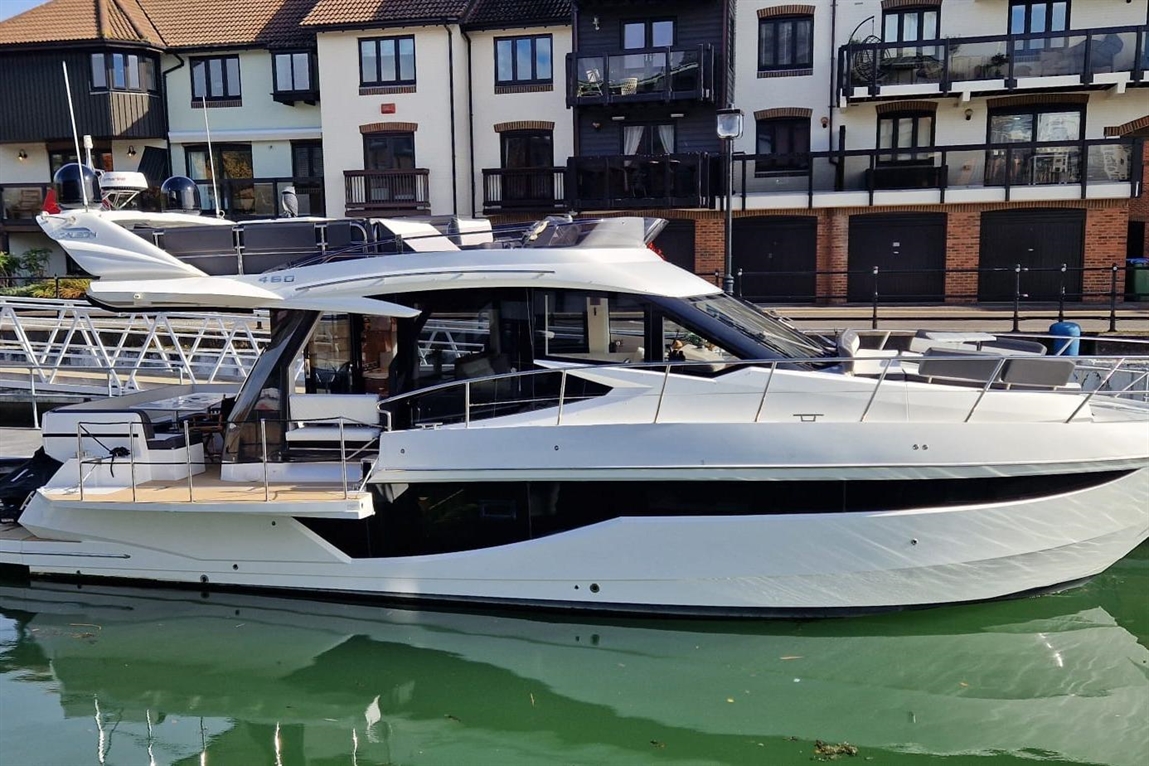 A luxury yacht docked at a marina, with modern design, glass windows, and reflection in the green water.